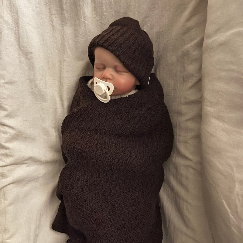 Newborn baby swaddled in brown blanket with matching hat in a bassinet