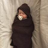 Newborn baby swaddled in brown blanket with matching hat in a bassinet