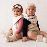Two babies in warm clothing sitting on a white background