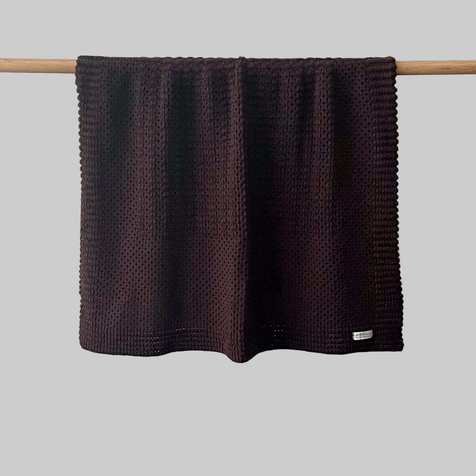 Textured brown bassinet blanket hanging on a wooden rod against a grey background
