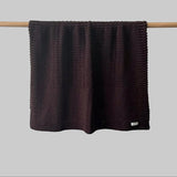 Textured brown bassinet blanket hanging on a wooden rod against a grey background