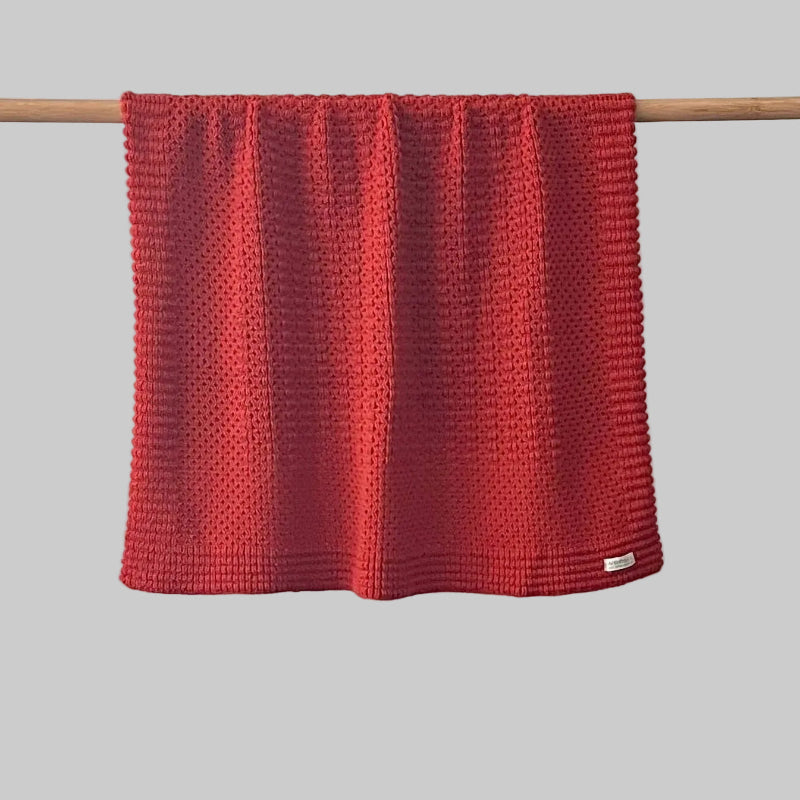 Textured burnt orange bassinet blanket hanging on a wooden rod against a grey background