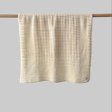 Textured buttermilk bassinet blanket hanging on a wooden rod against a grey background