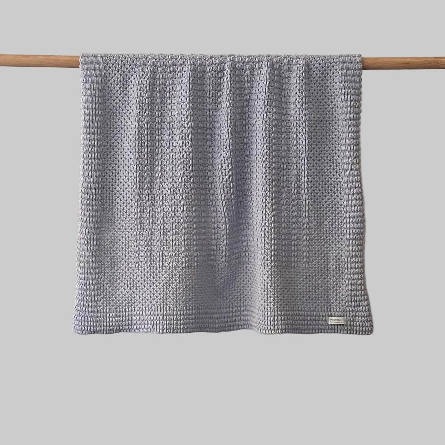 Textured misty blue bassinet blanket hanging on a wooden rod against a grey background