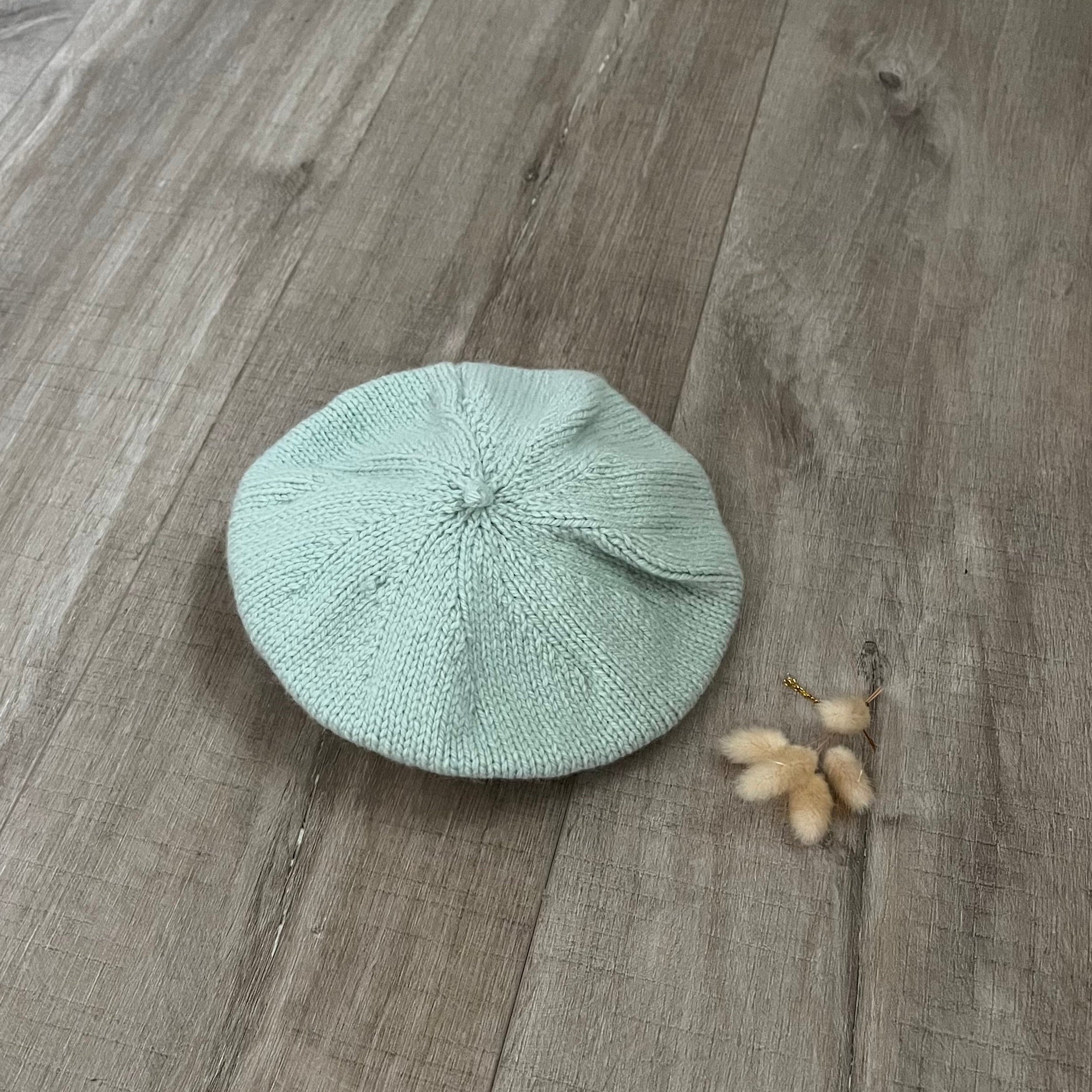 mint green beret on a wooden surface with dried flowers