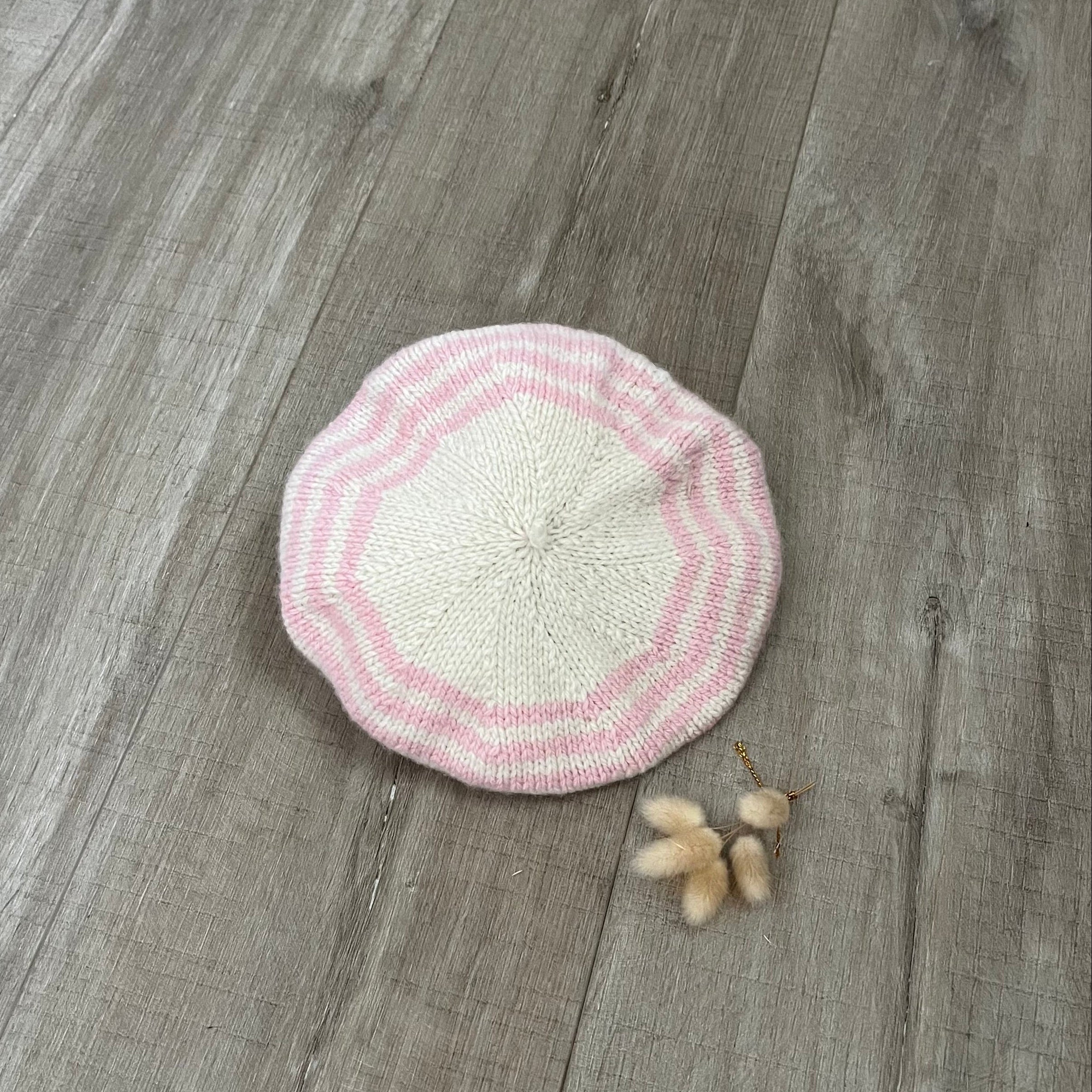 Pink and natural knitted beret on a wooden surface with dried flowers