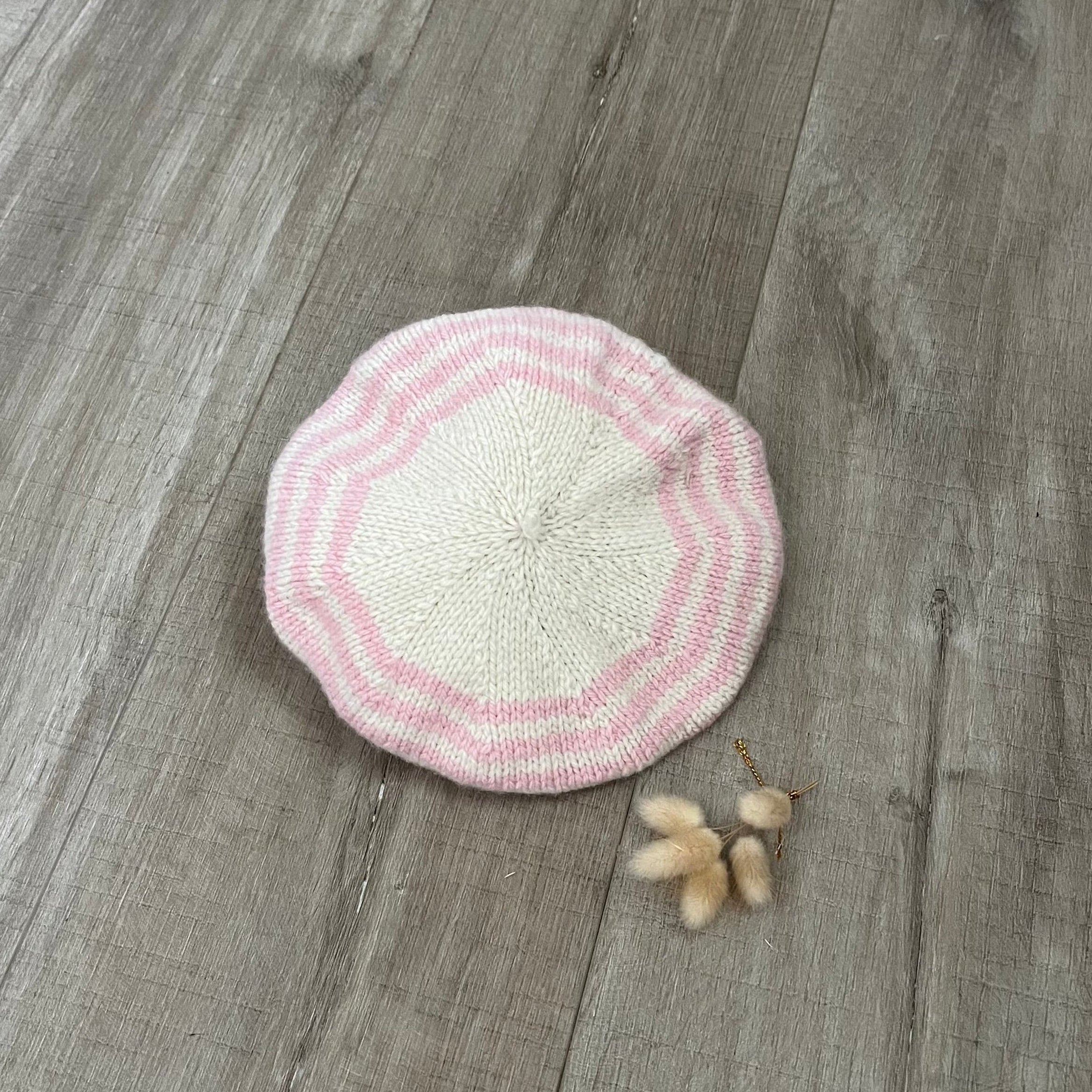 Pink and natural knitted beret on a wooden surface with dried flowers
