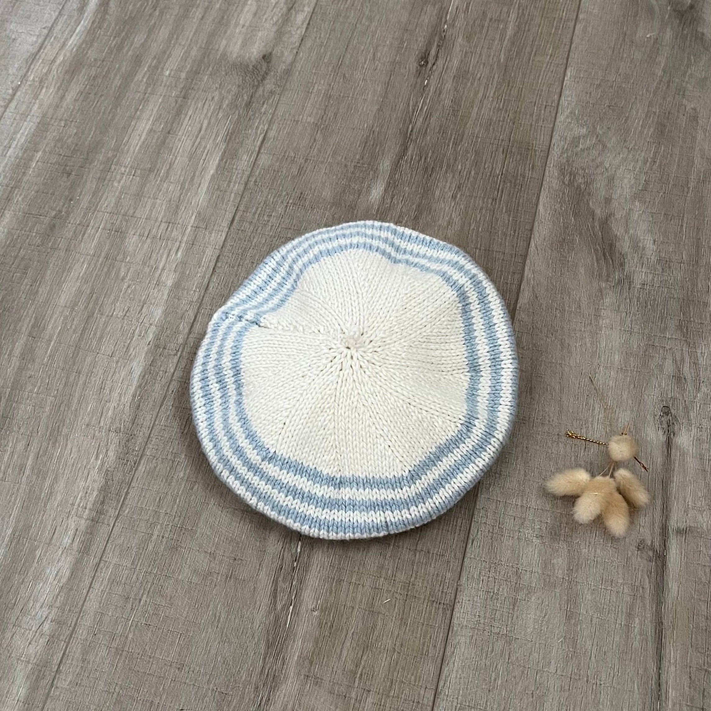 Knitted beret with blue and white stripes on a wooden surface