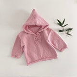 Pink knitted hoodie on a white surface with a green leaf decoration.