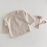 Natural baby sweater on a white surface with wooden toys.