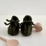 Forest green knitted baby booties with wooden rattle and spoon on a white background