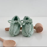 Pair of mint knitted baby shoes with wooden rattle and spoon on a white background