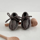 Knitted baby booties with wooden spoons on a white background
