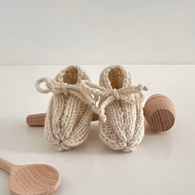 Knitted baby booties with wooden spoons on a light background