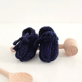 Navy blue baby booties with wooden rattle on a white background