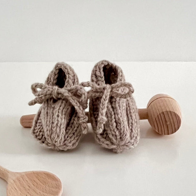 Knitted baby booties with wooden rattle and spoon on a white background