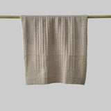Textured sandstone bassinet blanket hanging on a wooden rod against a grey background