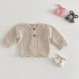 Natural coloured knitted baby cardigan on a light grey background