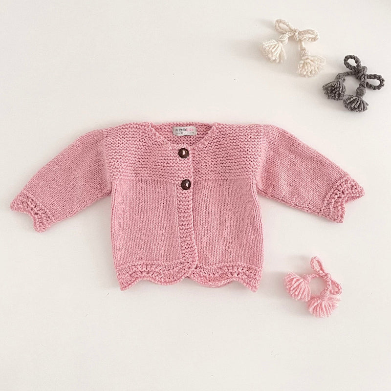Pink coloured knitted baby cardigan on a light grey background