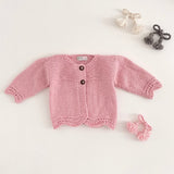 Pink coloured knitted baby cardigan on a light grey background
