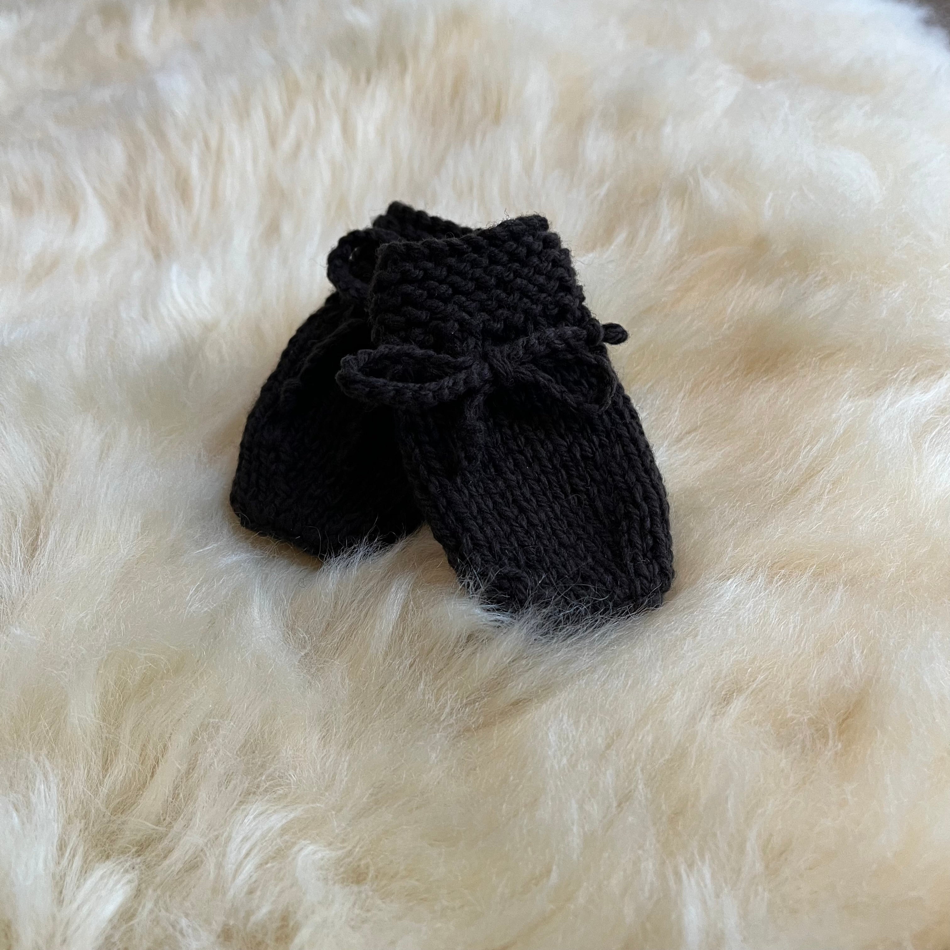 Pair of chocolate knitted baby mittens on a fluffy sheepskin rug