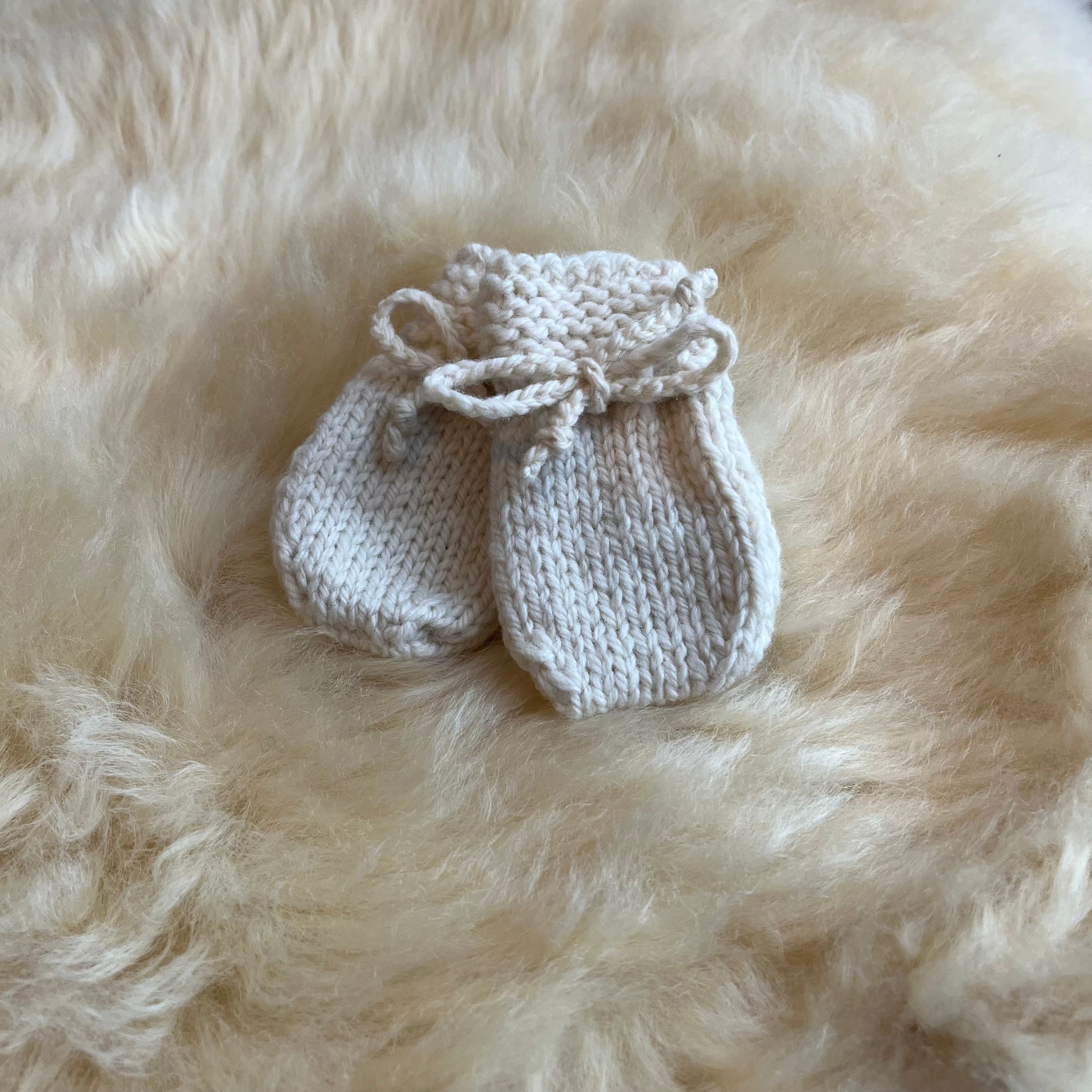 Pair of natural knitted baby mittens on a fluffy sheepskin rug