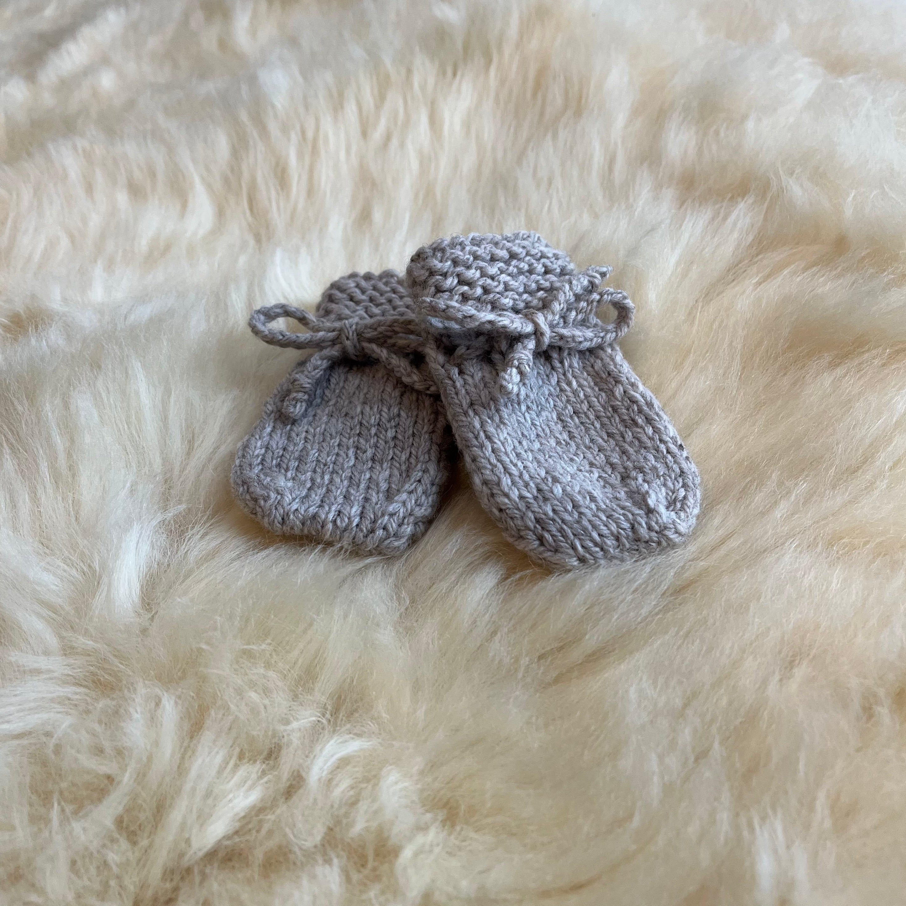 Pair of oatmeal knitted baby mittens on a fluffy sheepskin rug