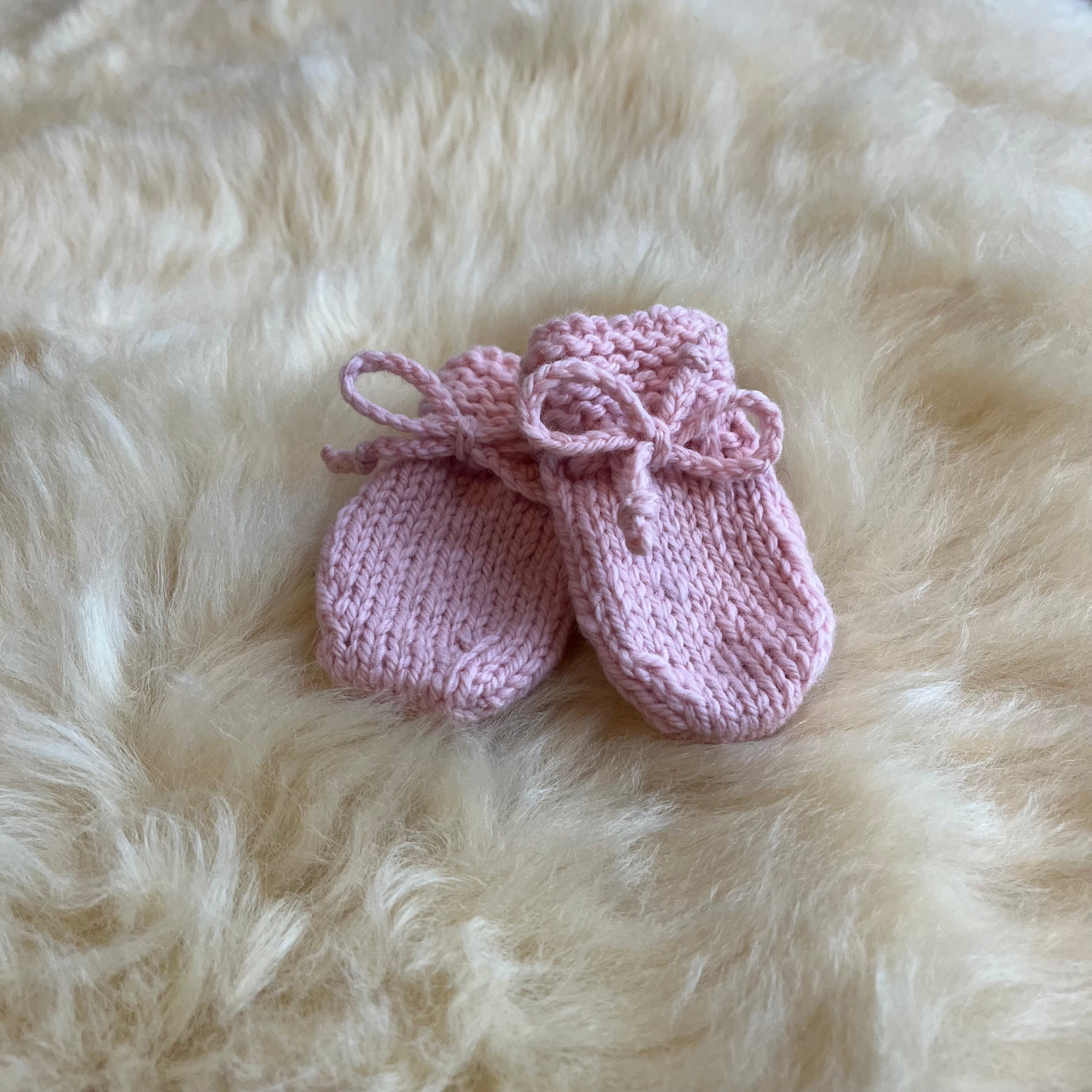 Pair of pink knitted baby mittens on a fluffy sheepskin rug