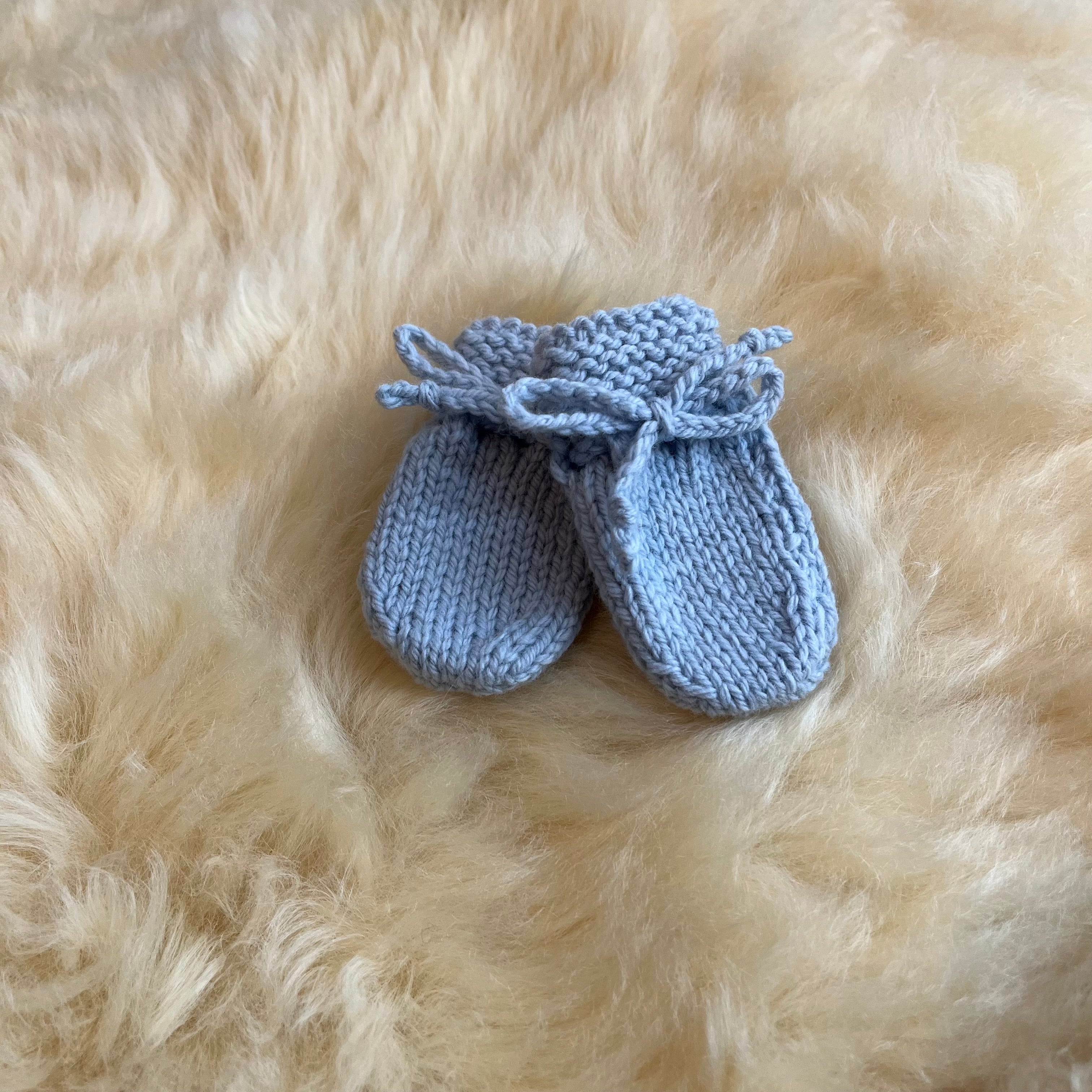 Pair of blue knitted baby mittens on a fluffy sheepskin rug