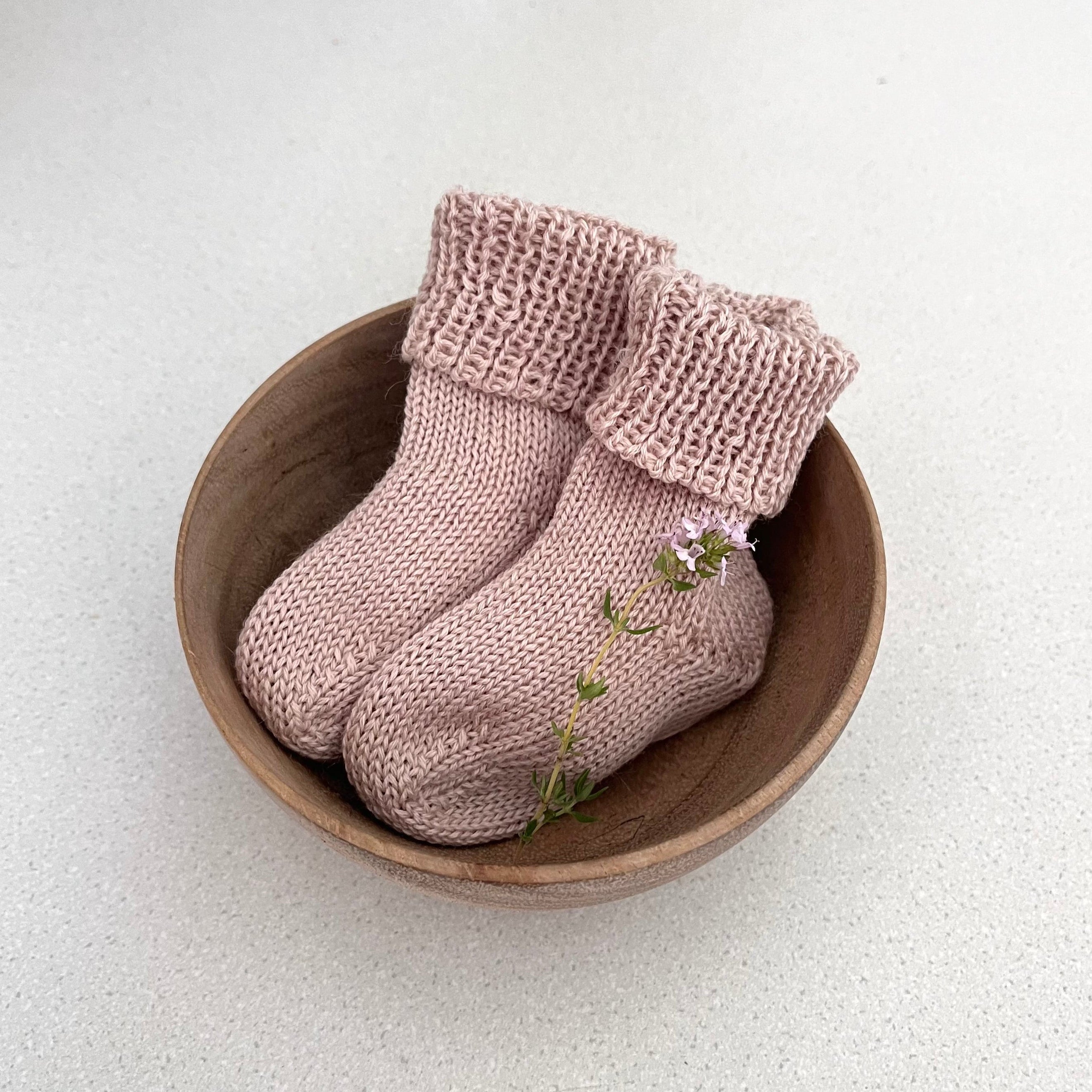 Pair of sandstone knitted baby socks in a wooden bowl on a light background