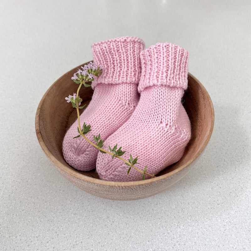 Pair of pink baby socks in a wooden bowl on a light background