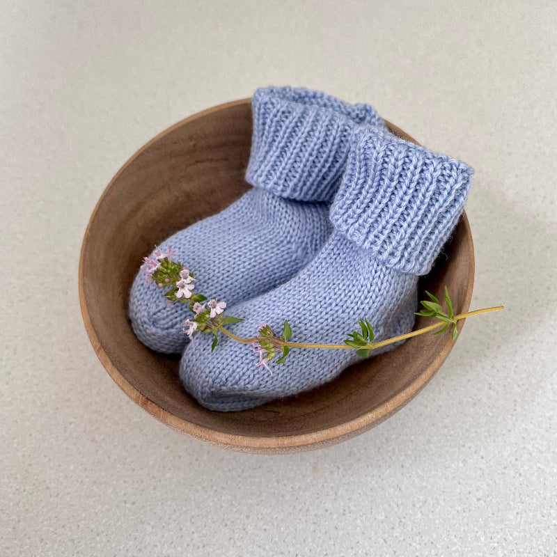 Pair of blue baby socks in a wooden bowl on a light background