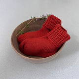 Pair of burnt orange baby socks in a wooden bowl on a light background