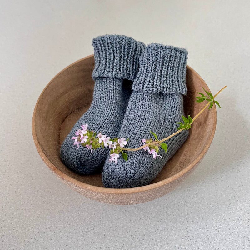 Pair of dusky blue baby socks in a wooden bowl on a light background