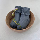 Pair of dusky blue baby socks in a wooden bowl on a light background