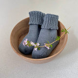Pair of dusky blue baby socks in a wooden bowl on a light background