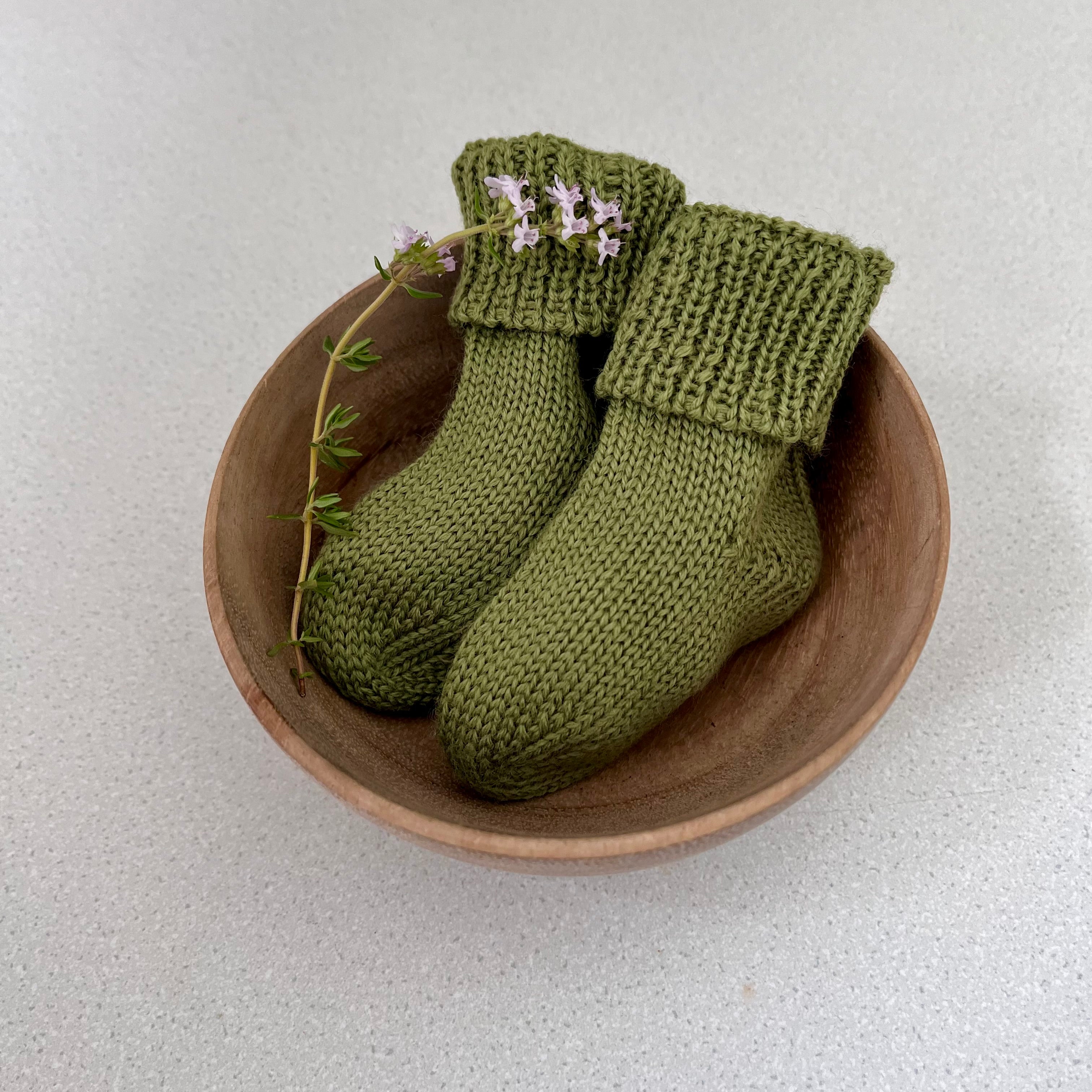 Pair of moss baby socks in a wooden bowl on a light background