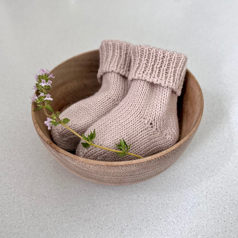 Pair of sand baby socks in a wooden bowl on a light background