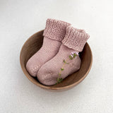 Pair of warm sandstone baby socks in a wooden bowl on a light background