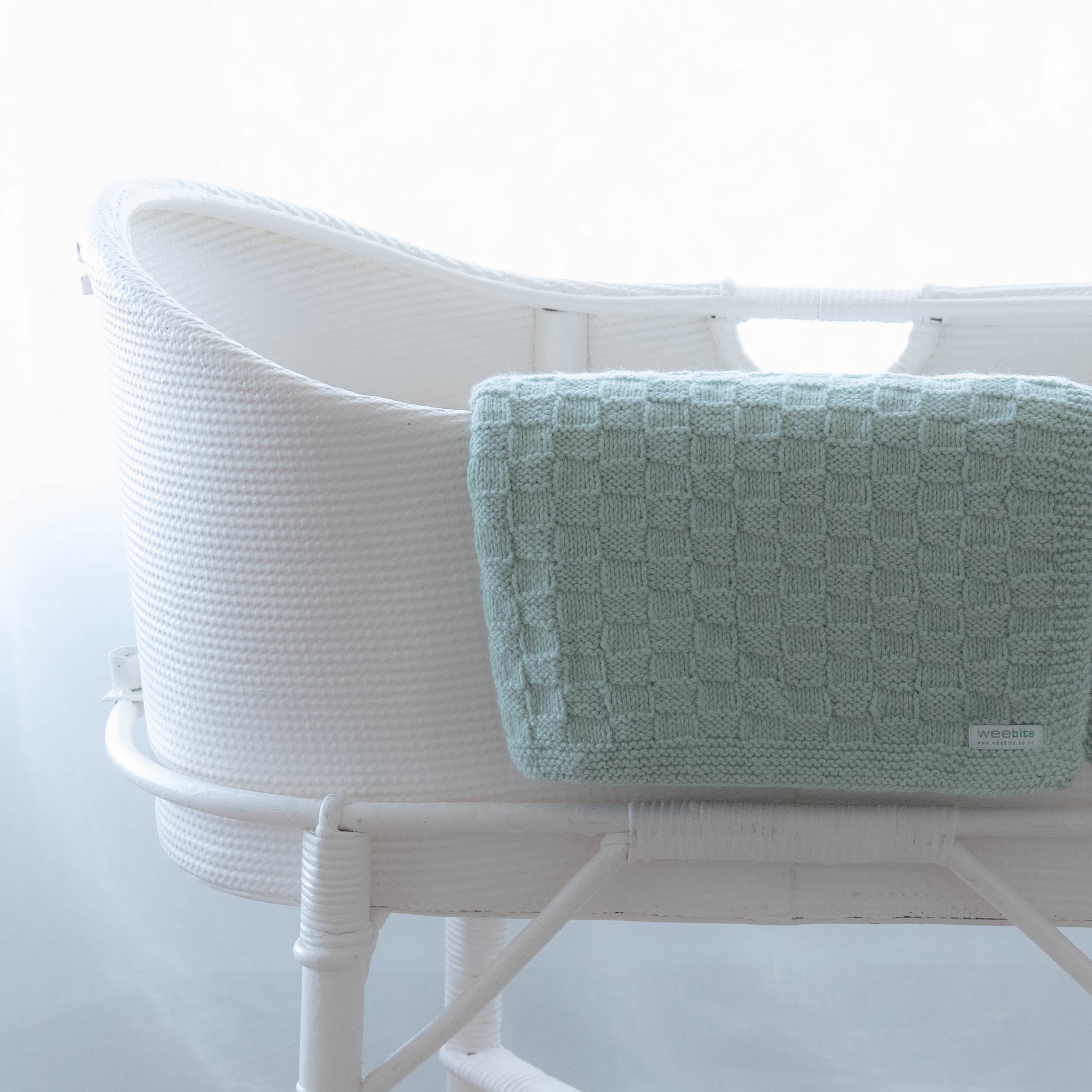 White woven bassinet with a light green textured blanket on a white background
