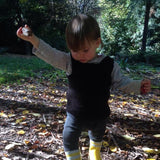 Child in a forest setting holding a small object wearing brown singlet vest