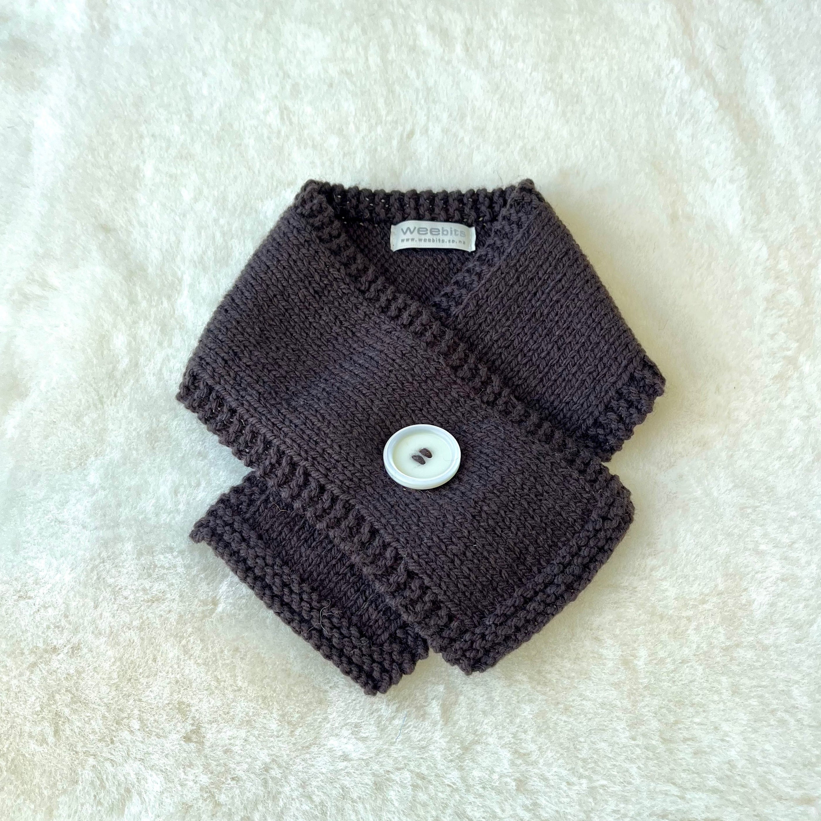 A brown knitted baby scarf with a white button closure, laid flat on a white textured faux fur background.