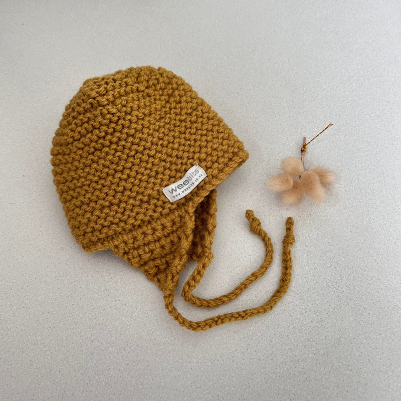 Knitted chunky knit baby hat mustard colour on a light grey background
