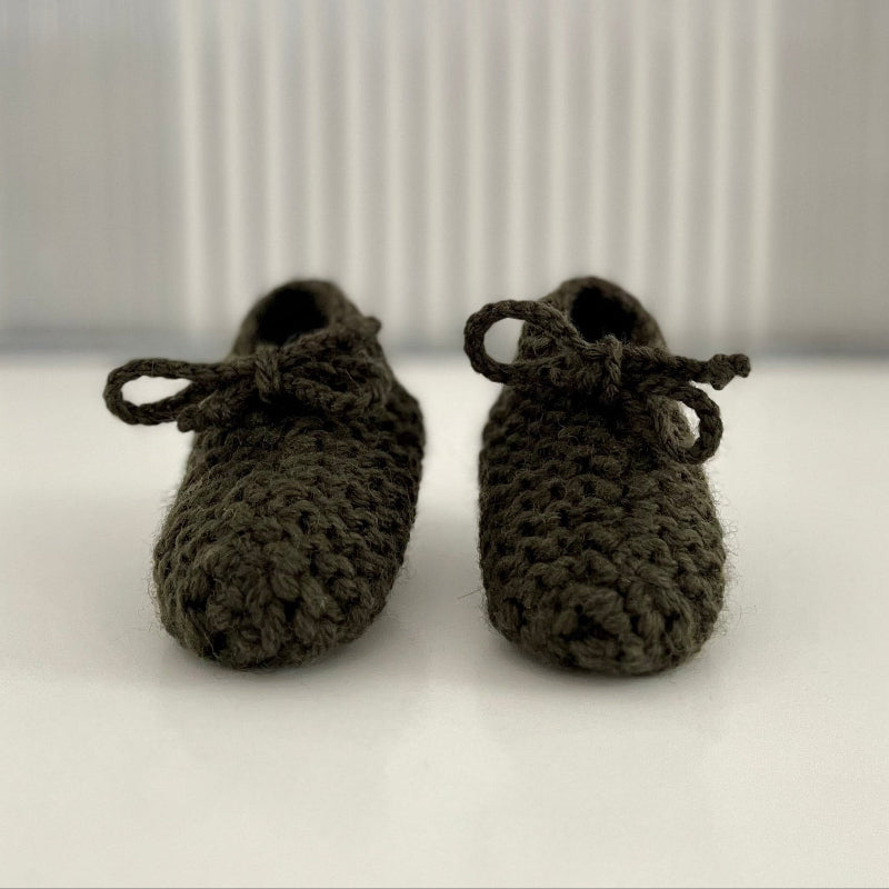Pair of forest green baby chunky knit booties on a white surface with a striped background