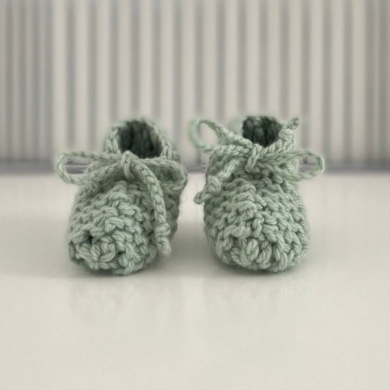 Pair of mint baby chunky knit booties on a white surface with a striped background
