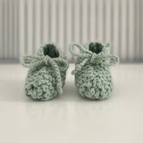 Pair of mint baby chunky knit booties on a white surface with a striped background