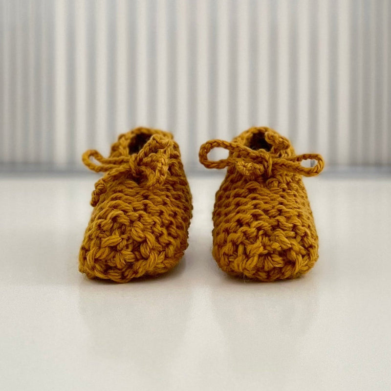 Pair of mustard baby chunky knit booties on a white surface with a striped background