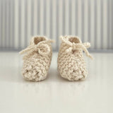 Pair of natural baby chunky knit booties on a white surface with a striped background