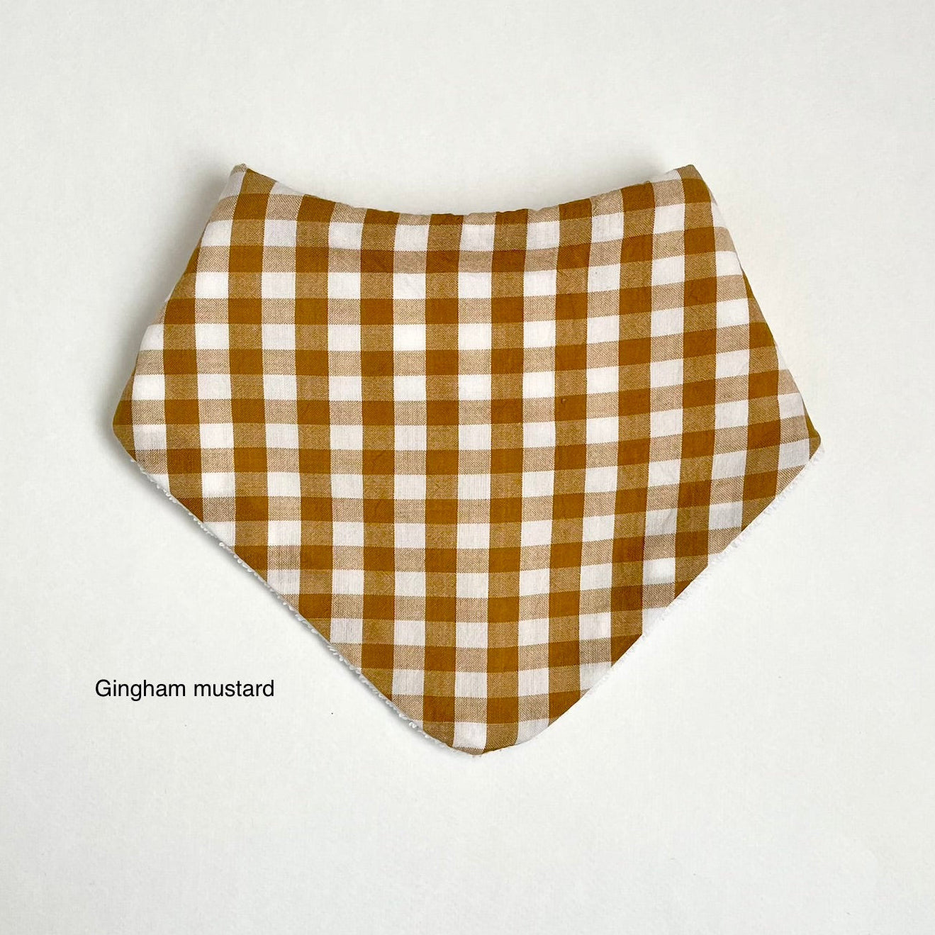 A triangular bandana-style bib or scarf with a gingham check pattern in mustard yellow and white, displayed flat against a light gray background with the text 'Gingham mustard' underneath.