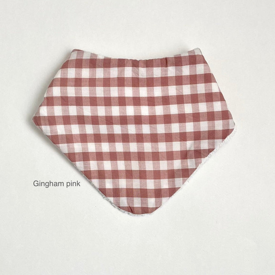 A pink and white gingham checkered bandana bib laid flat on a light off-white background, with the text 'Gingham pink' printed below it.